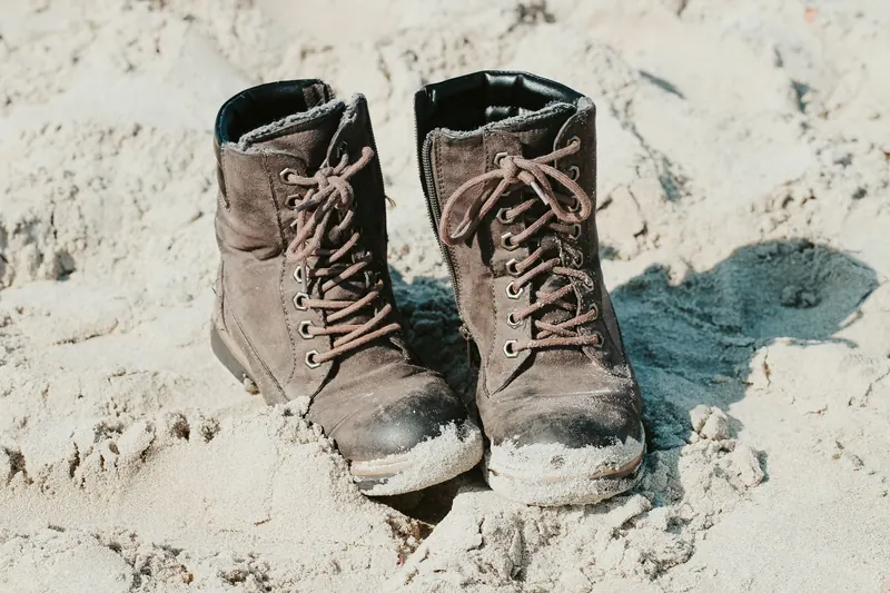 Close-up of worn leather boots on sandy outdoor ground, conveying adventure