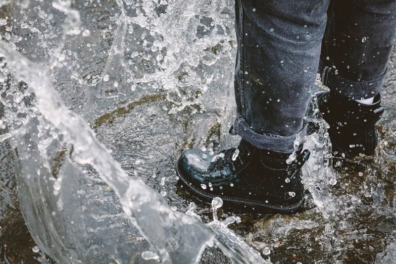 A close-up of a person stomping in water with waterproof boots, capturing a playful splash