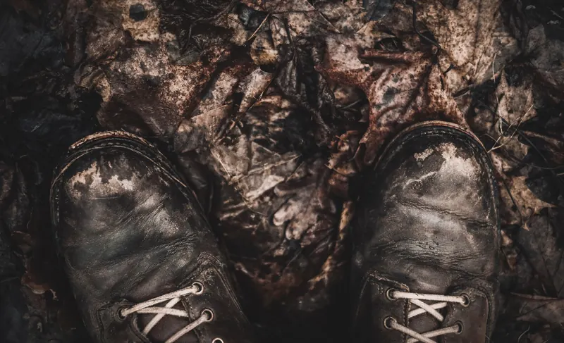 Close-up of worn leather boots on fallen autumn leaves, highlighting outdoor exploration