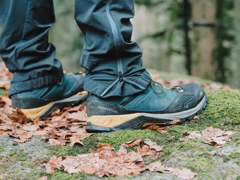 Close-up of hiking boots surrounded by fallen leaves on a mossy path in the forest during autumn