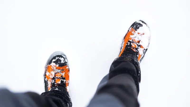 Orange winter boots covered in snow, viewed from above, on a snowy day