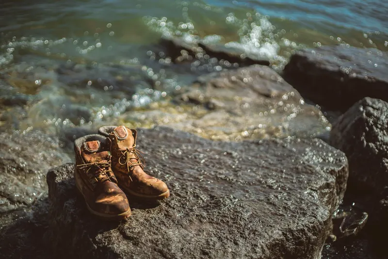 Abandoned hiking boots on a rocky shoreline with waves crashing in